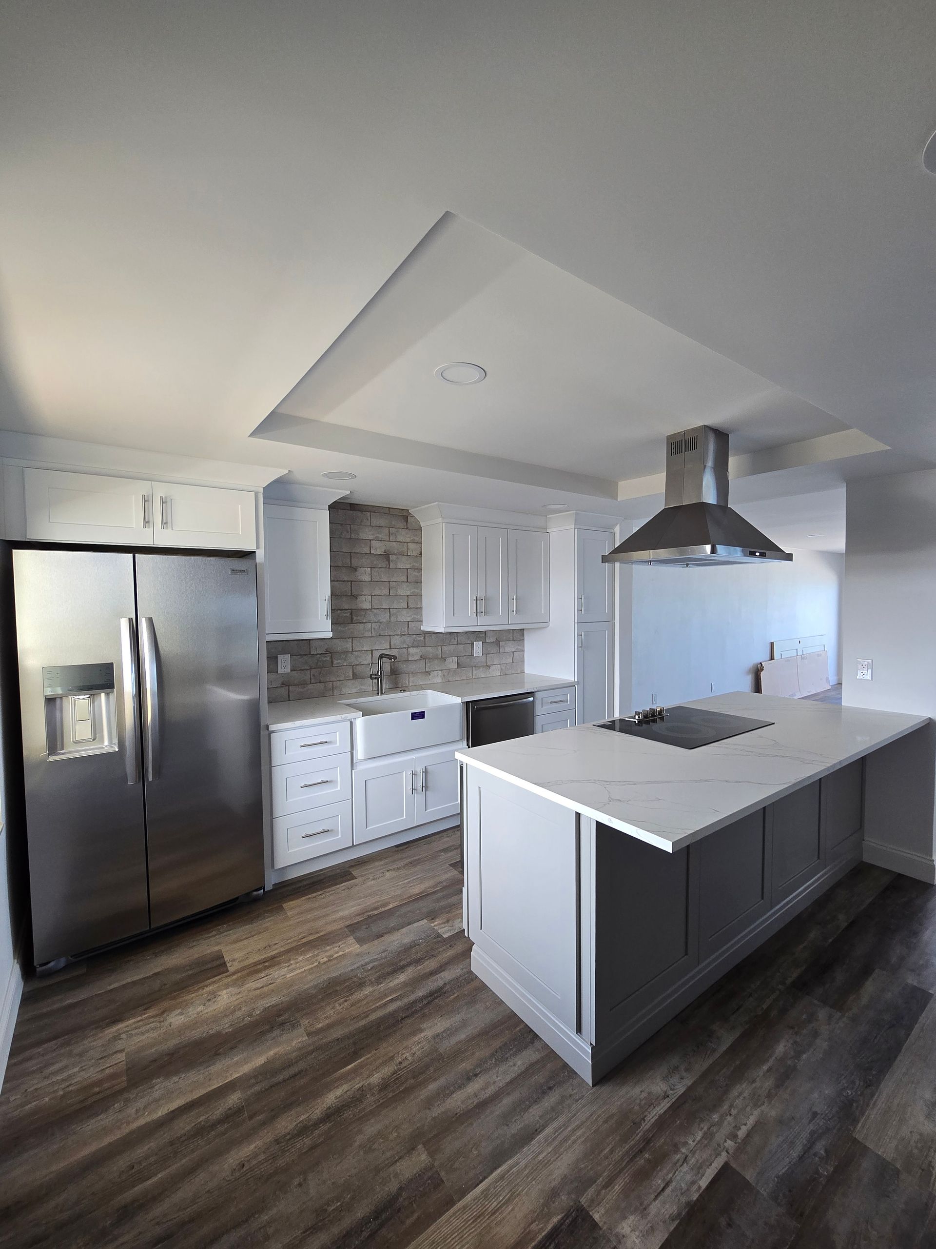 Modern kitchen featuring white cabinets, a stone backsplash, and a large island with a cooktop. Serving Ruskin