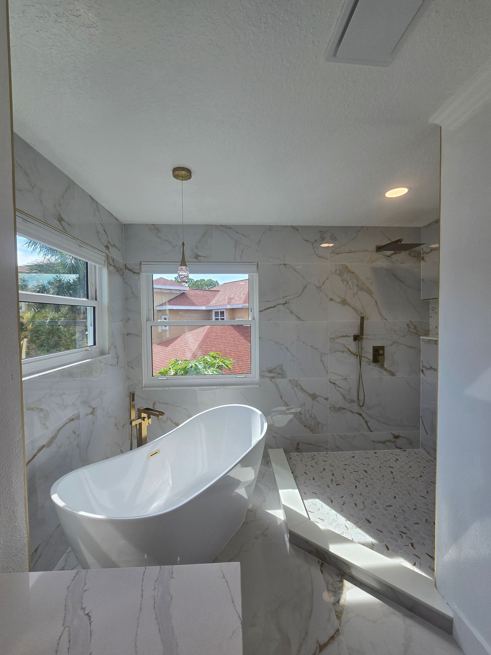 A modern bathroom featuring a white freestanding tub, gold faucet, marble walls, and a shower. Serving homes in Odessa