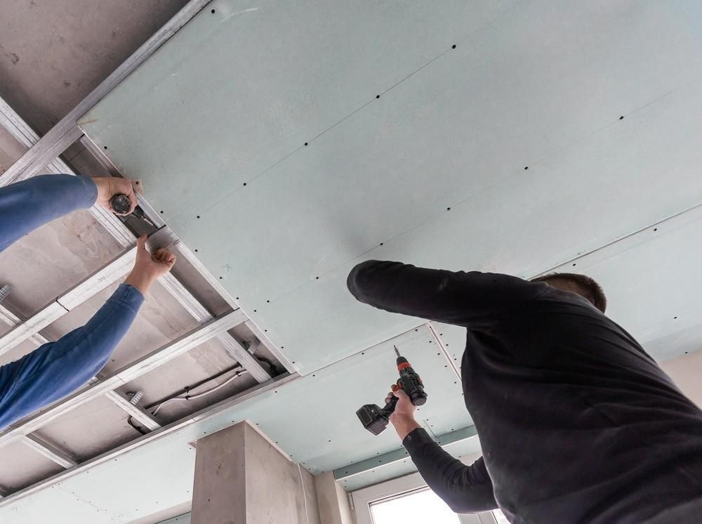 two men are working on a ceiling with a drill .