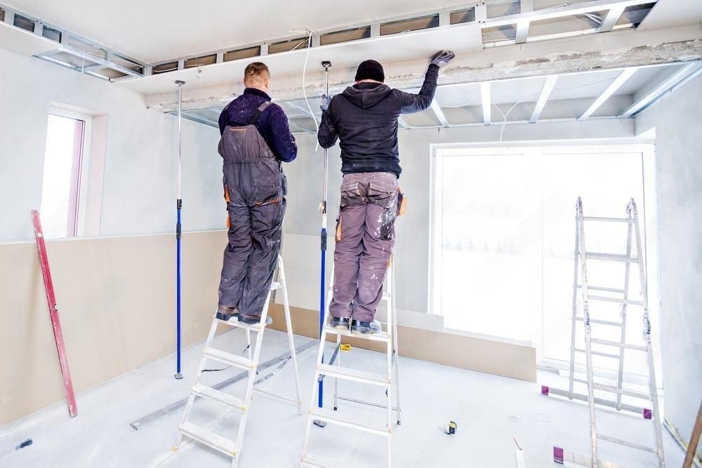 two men are working on a ceiling in a room .
