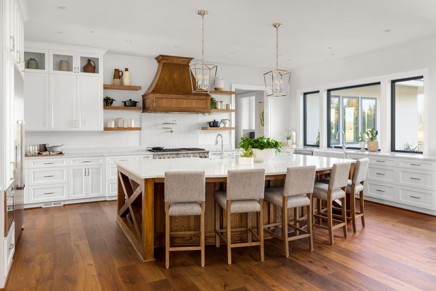 a kitchen with white cabinets , wooden floors , a large island and stools .