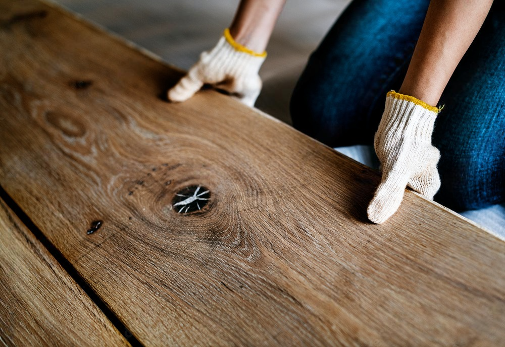 a person wearing gloves is installing a wooden floor .