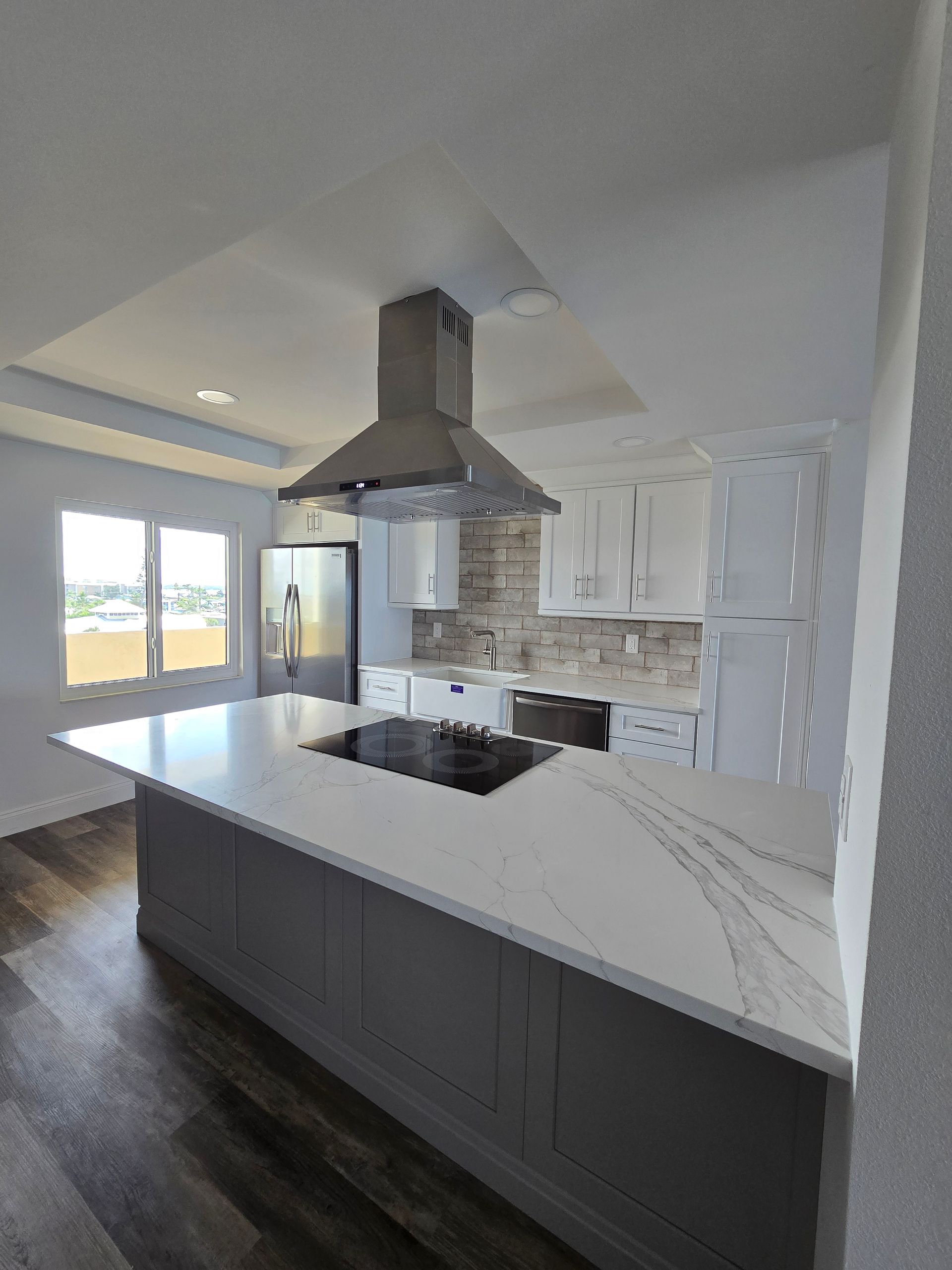 A kitchen with a dark grey island, white quartz countertop, black stovetop, range hood. Serving Kissimmee homeowners