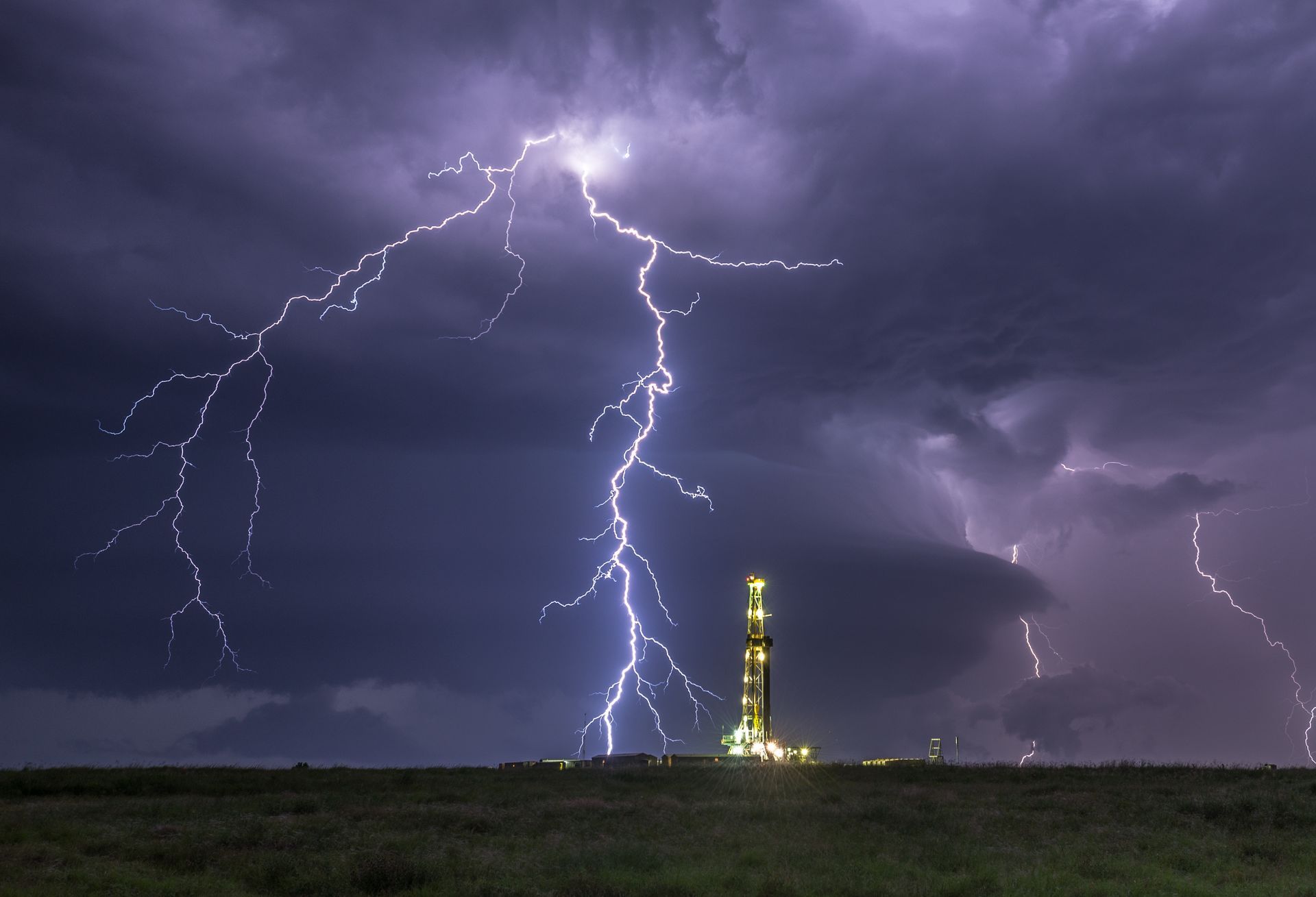 A bolt of lightning hits the ground in an open plain next to an electrical tower