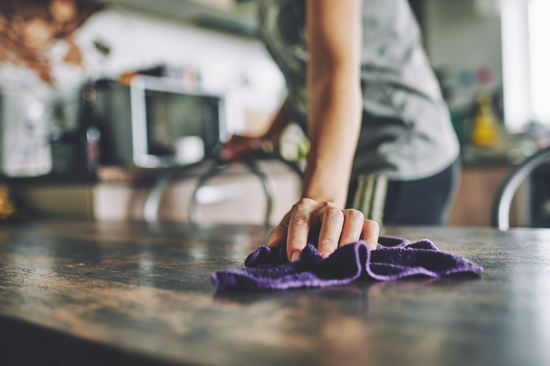 A woman is cleaning a table with a purple cloth.