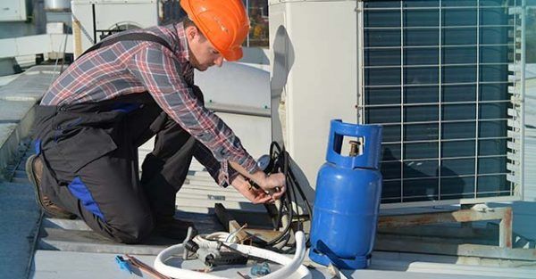 A man wearing a hard hat is working on an air conditioner.