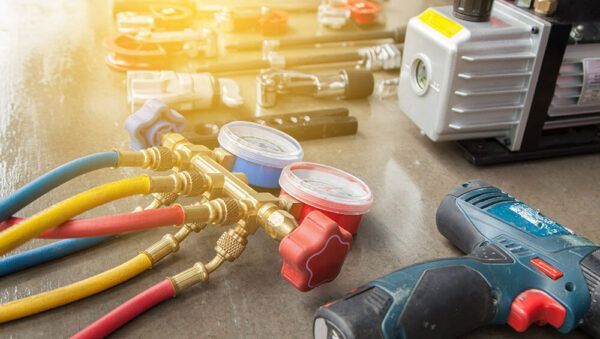 A drill , gauges , hoses and a vacuum pump are on a table.