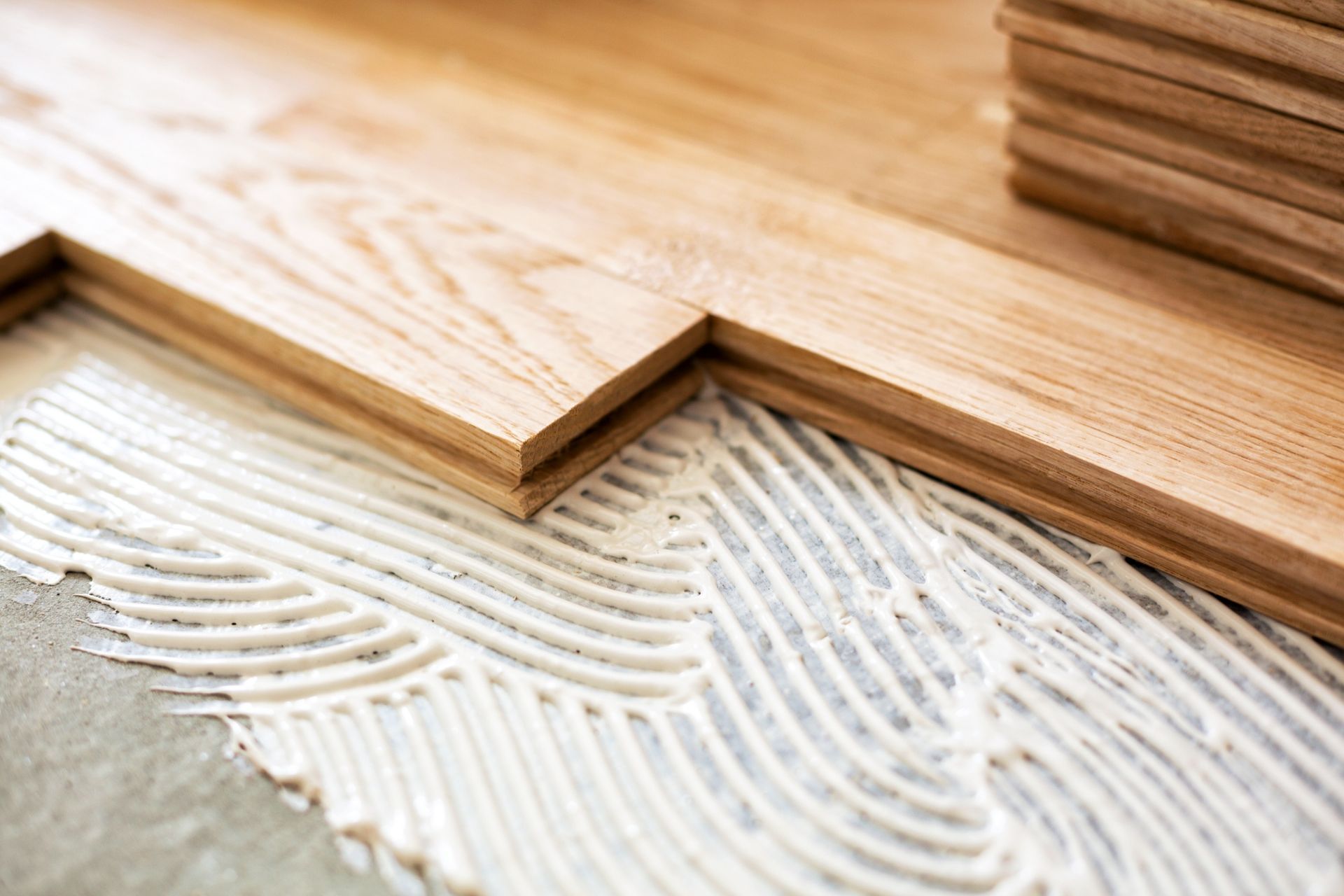 Wooden floor planks being laid over gray adhesive with visible trowel ridges