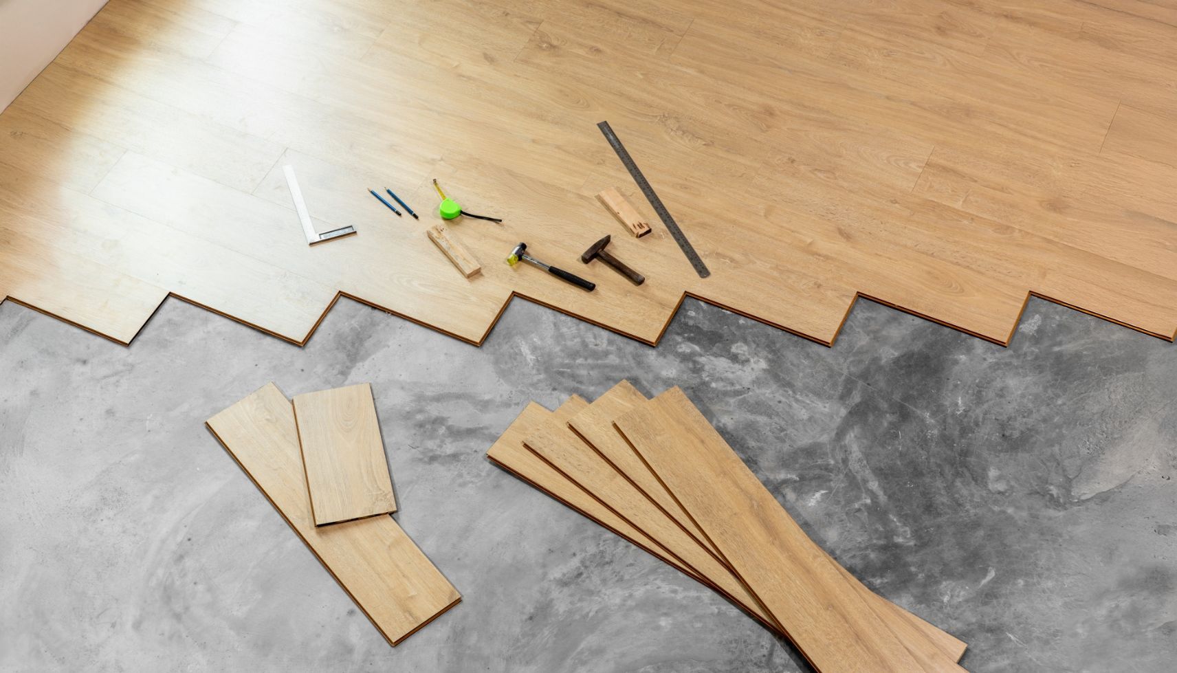 Wooden parts, small nails, and tools laid out on a workbench next to a gray floor panel edge.