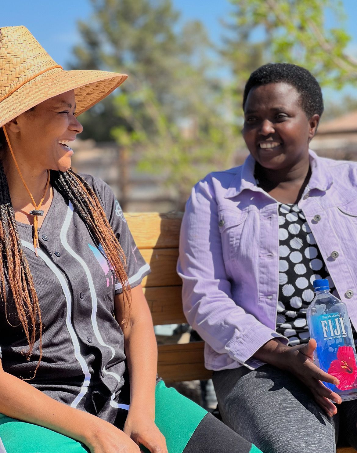 Two women are sitting on a bench and one is holding a bottle of fiji water.
