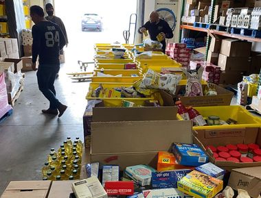People sorting food in a warehouse. Boxes and bins filled with canned goods, snacks and drinks.