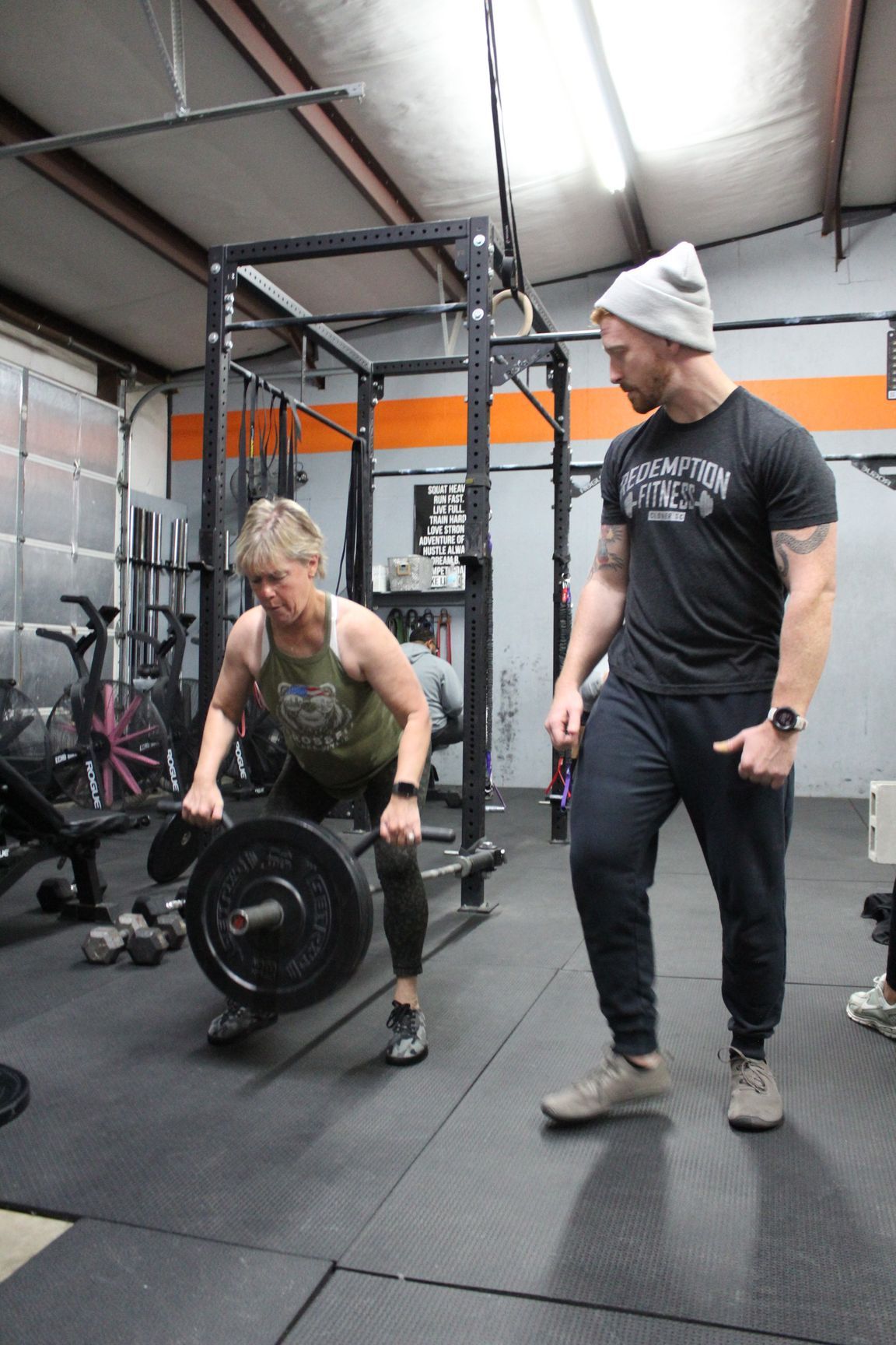 Two people in a gym preparing to lift a barbell on a rubber mat floor