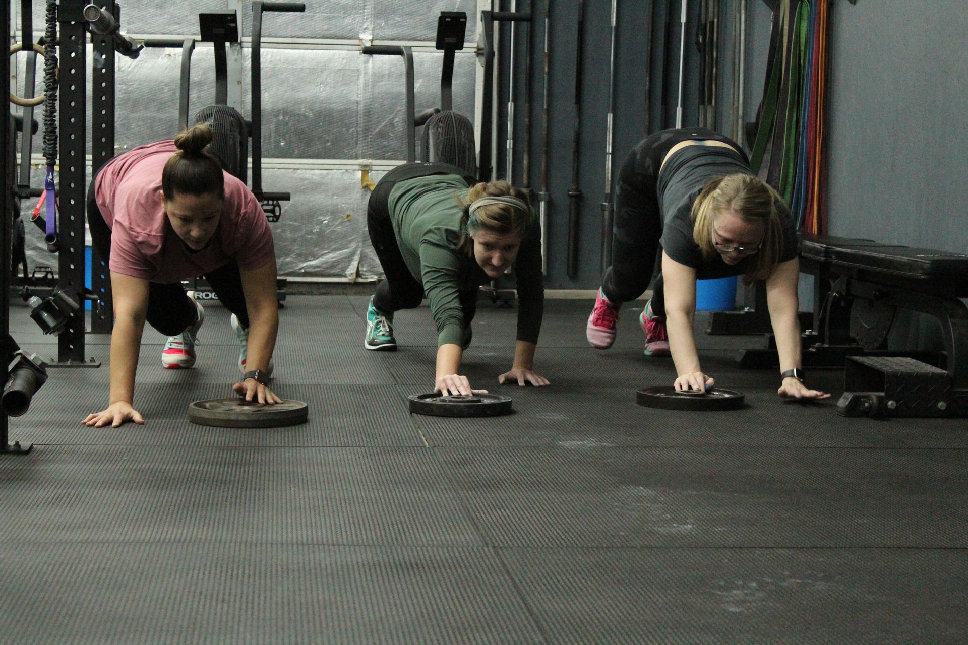 Three people in workout clothes in a plank position on gym floor mats.