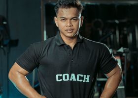 Man in black “COACH” polo standing in a gym with hands on hips
