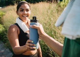 Woman smiling outdoors while receiving a water bottle in a grassy field