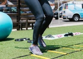 Person stepping through agility ladder on grass, wearing black leggings and gray sneakers.