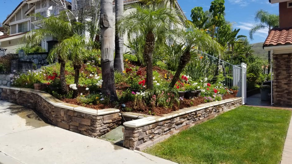 A house with a lush green lawn and a stone wall in front of it.