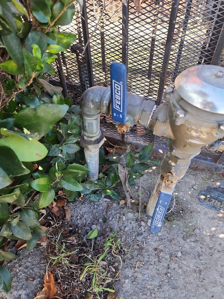 A water valve with a blue handle is sitting next to a fence.