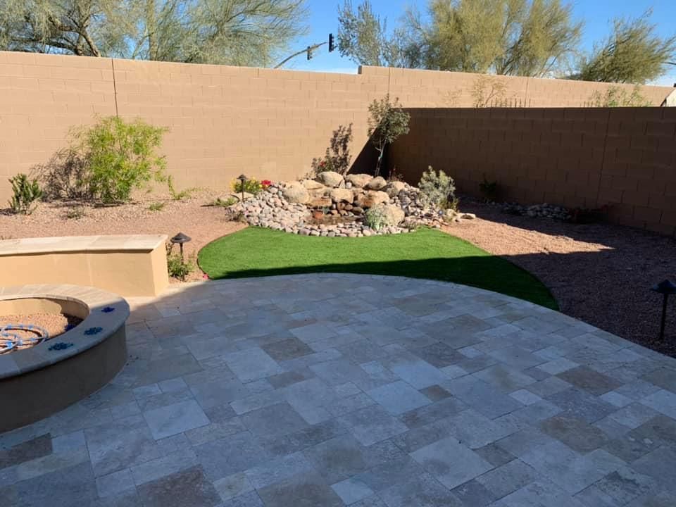 A patio with a fire pit and a waterfall in the backyard.