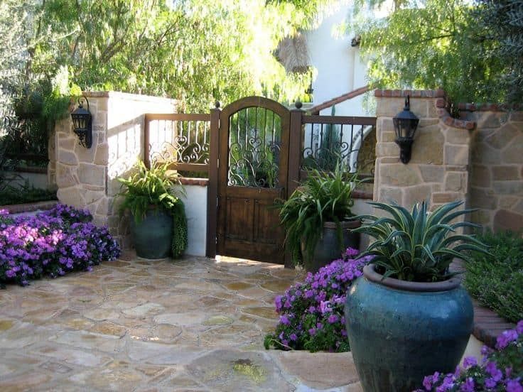 A wooden gate is surrounded by potted plants and purple flowers