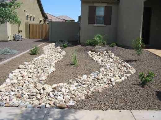 A yard with a lot of rocks and plants in front of a house.