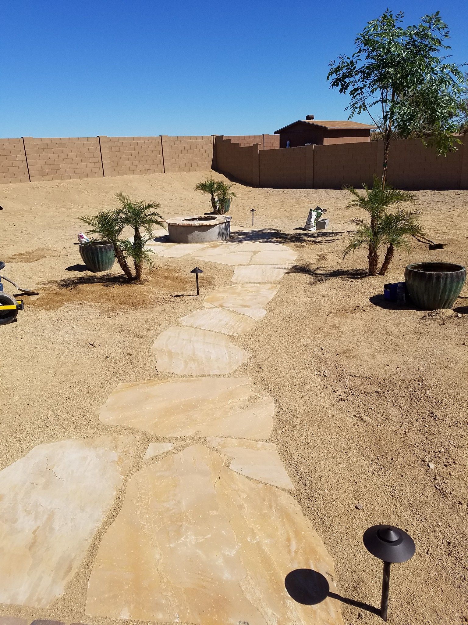 A stone walkway leading to a fire pit in the middle of a dirt field.