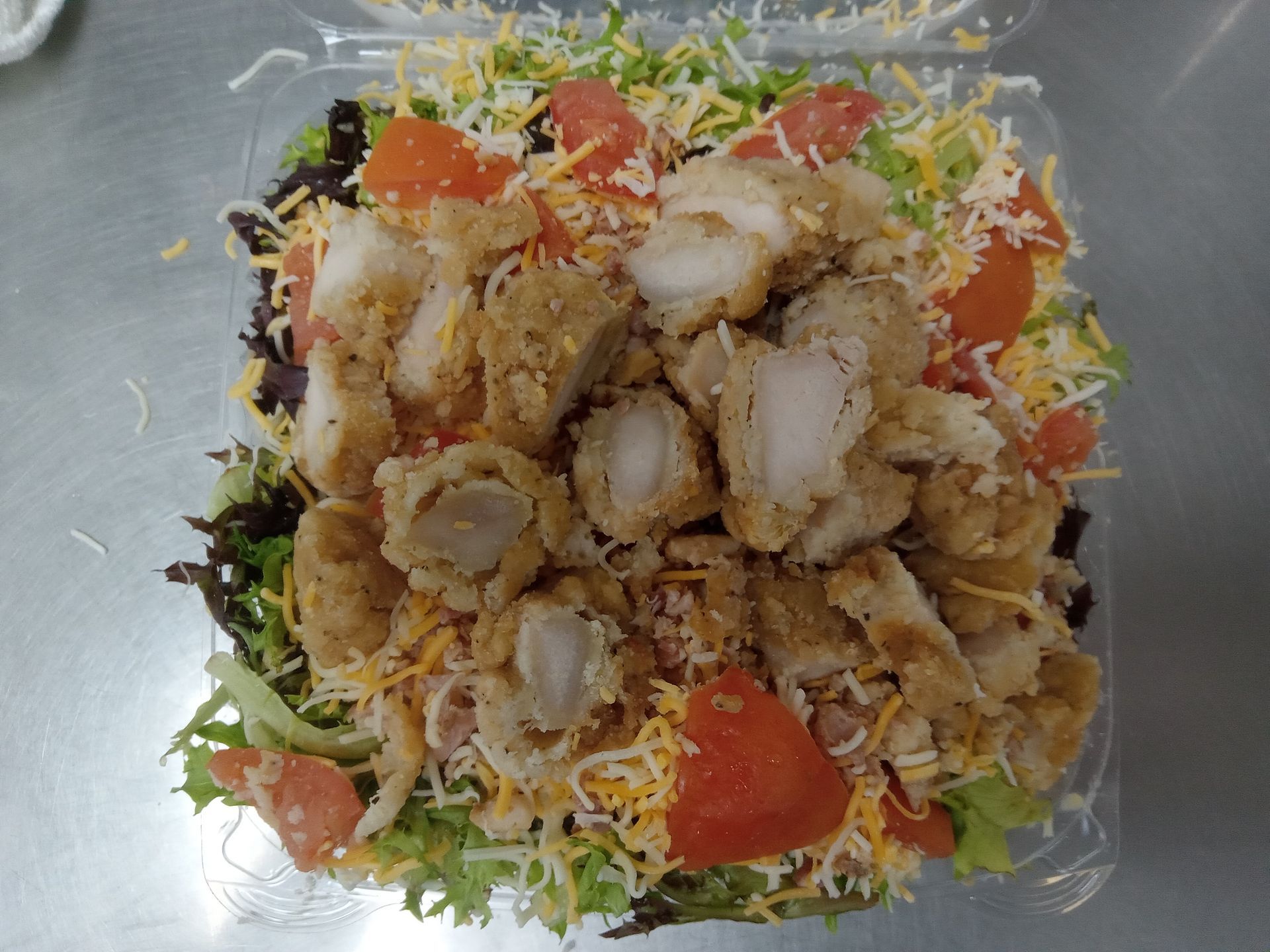A salad with chicken , tomatoes , cheese and lettuce in a plastic container.