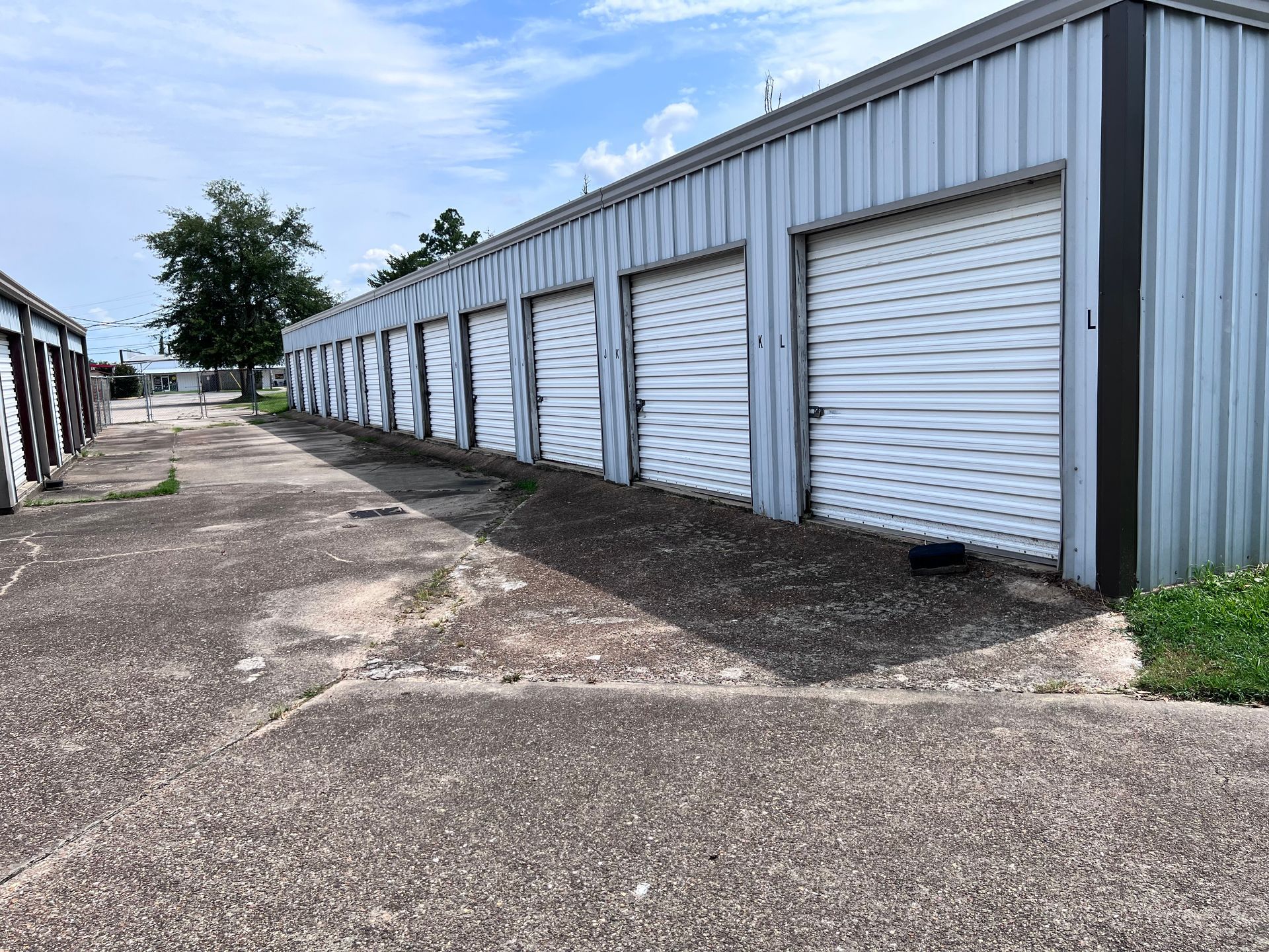 Row of white storage units with roll-up doors. A concrete path runs along the units.