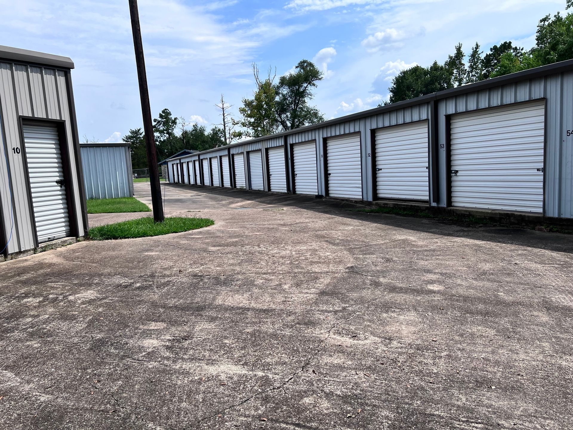 Row of storage units with white roll-up doors on a concrete lot under a cloudy sky.