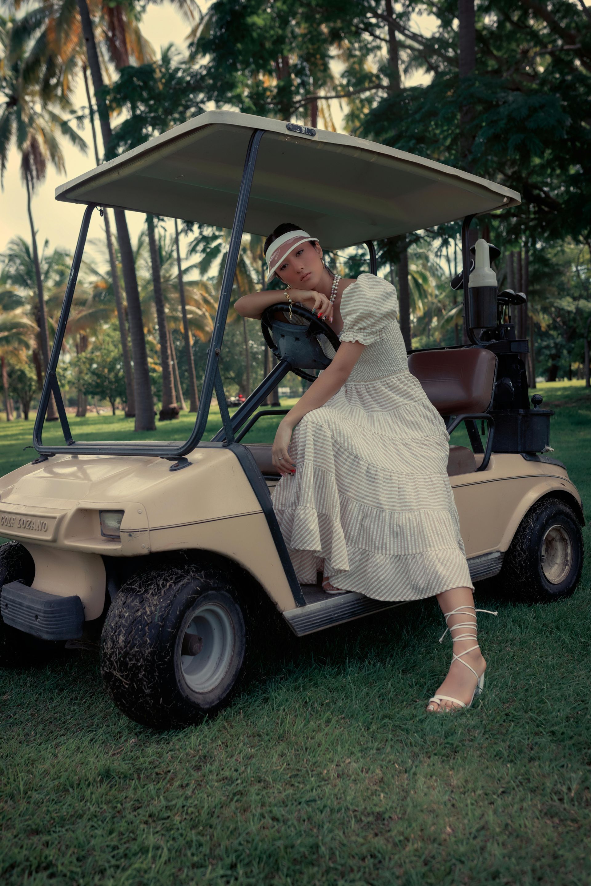 A woman in a white dress is sitting in a golf cart.