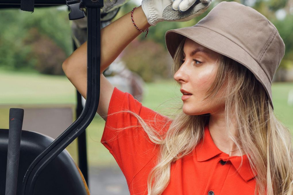 A woman wearing a hat and gloves is sitting in a golf cart.
