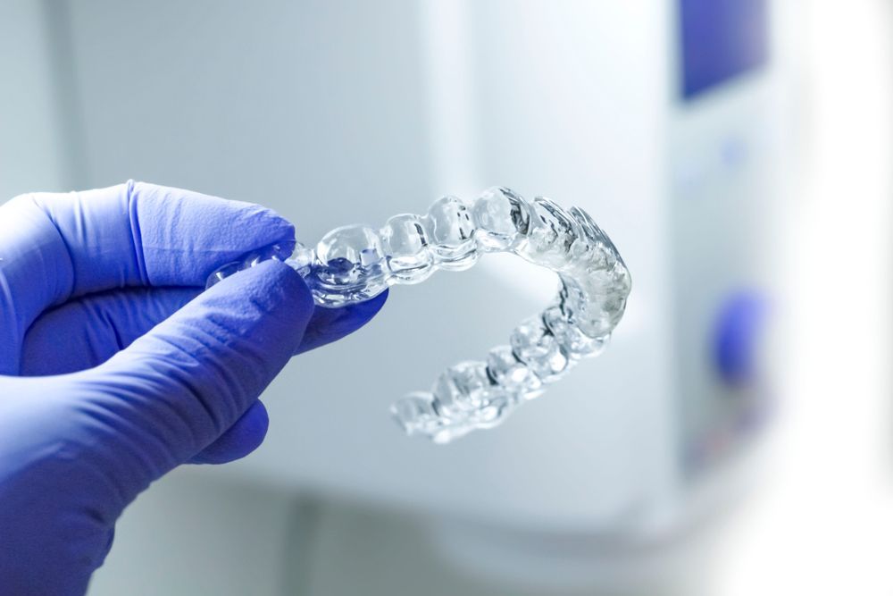 Hand in blue glove holding clear Invisalign aligner in dental office. — Trower Dental In Casuarina, NT
