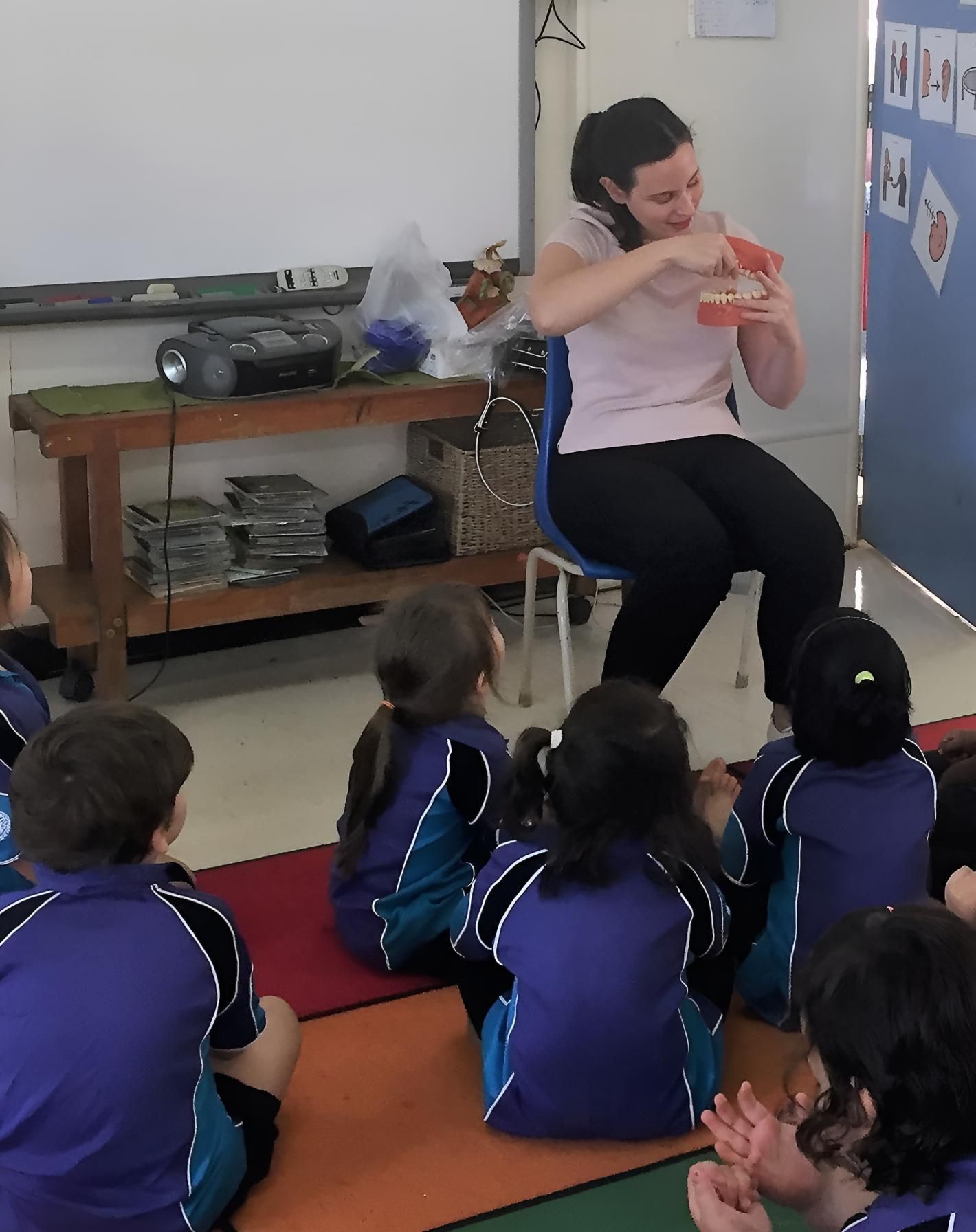 A Woman Sits in a Chair Reading a Book to a Group of Children — Trower Dental In Casuarina, NT