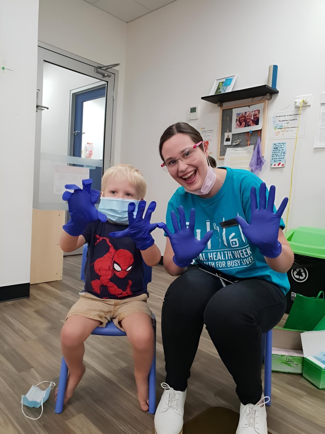 A Woman is Sitting Next to a Young Boy Wearing a Mask and Gloves — Trower Dental In Casuarina, NT