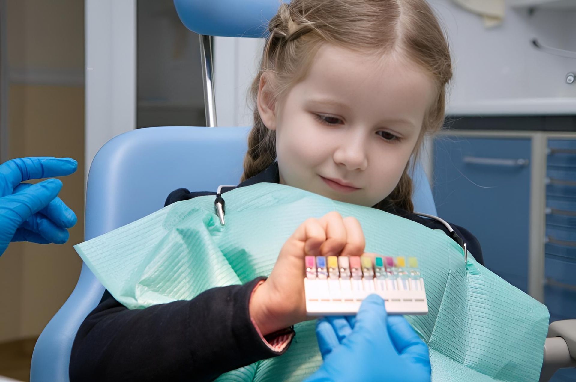 A Little Girl is Sitting in a Dental Chair Holding a Tooth Colour Chart — Trower Dental In Casuarina, NT