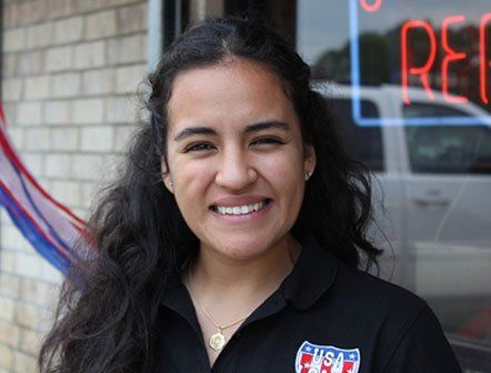 A woman wearing a usa shirt is smiling in front of a neon sign