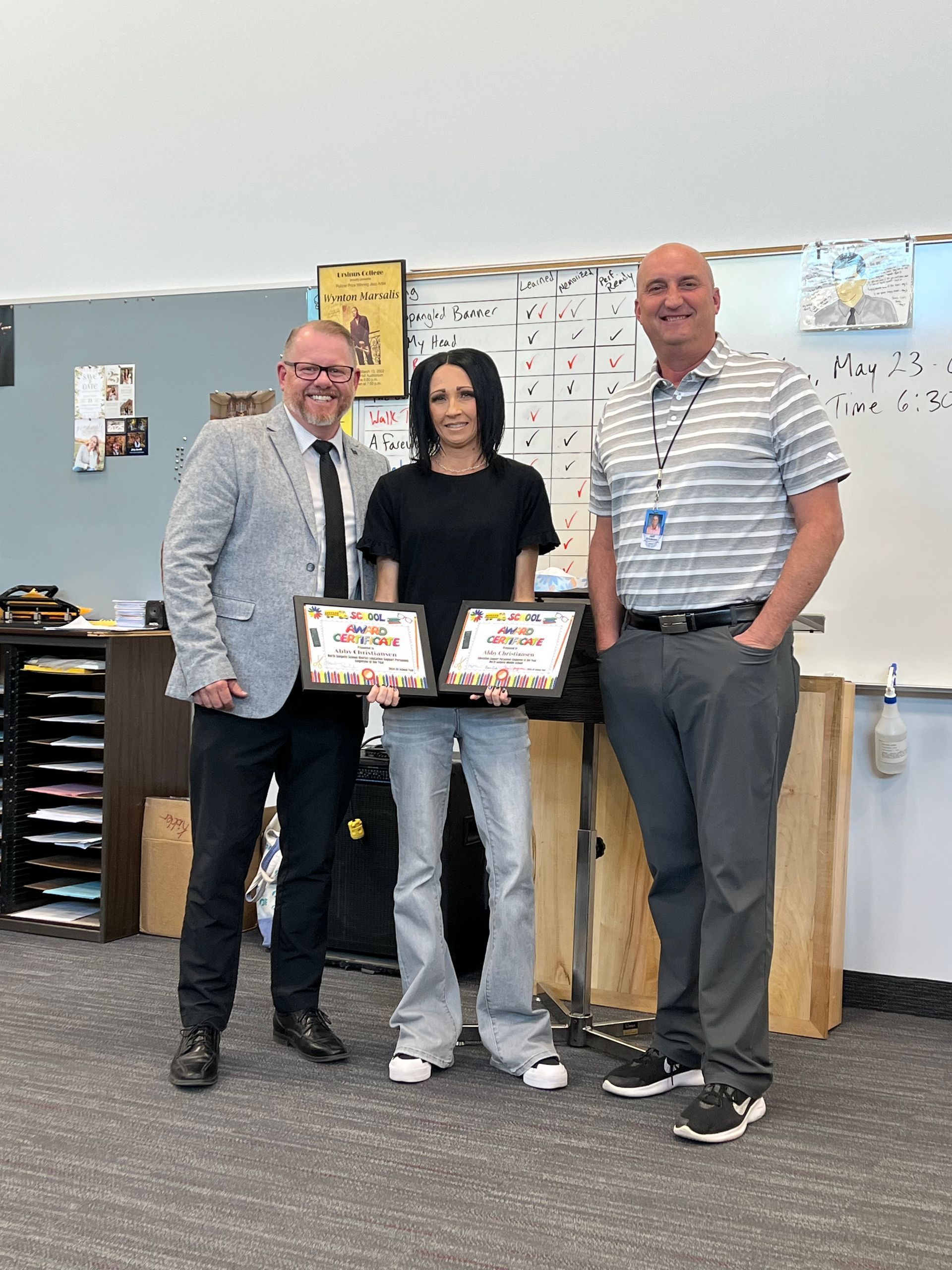 Two men and a woman are standing next to each other in a classroom holding certificates.