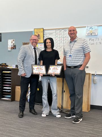 Two men and a woman are standing next to each other in a classroom holding certificates.
