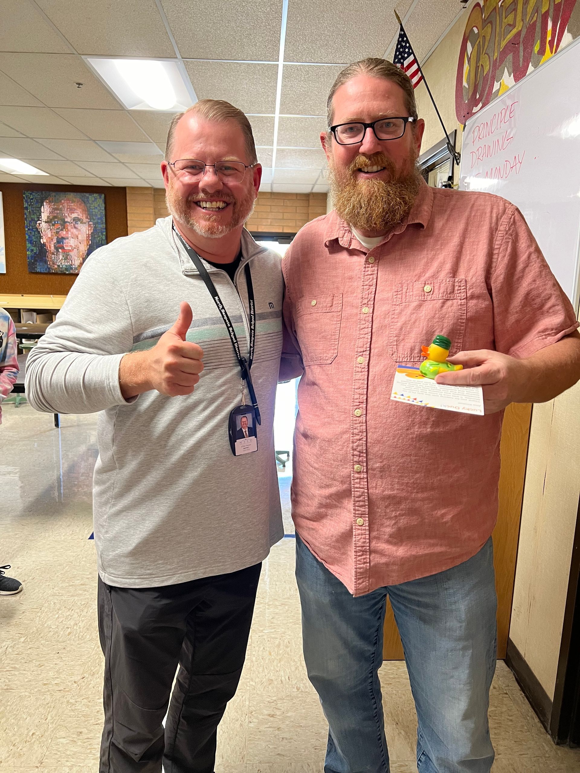 Two men are standing next to each other in a room giving a thumbs up.