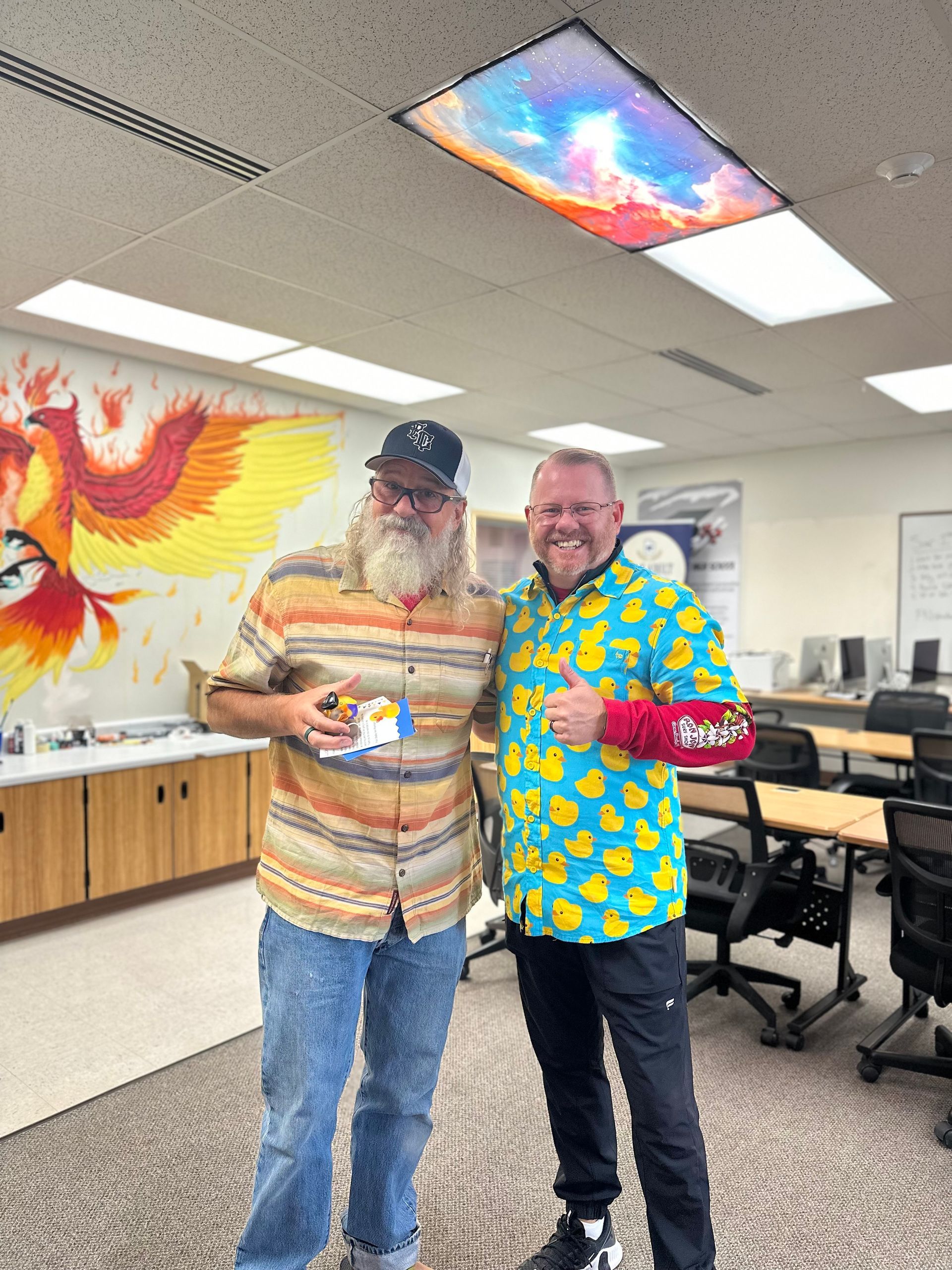 Two men are standing next to each other in a room with a mural on the wall.