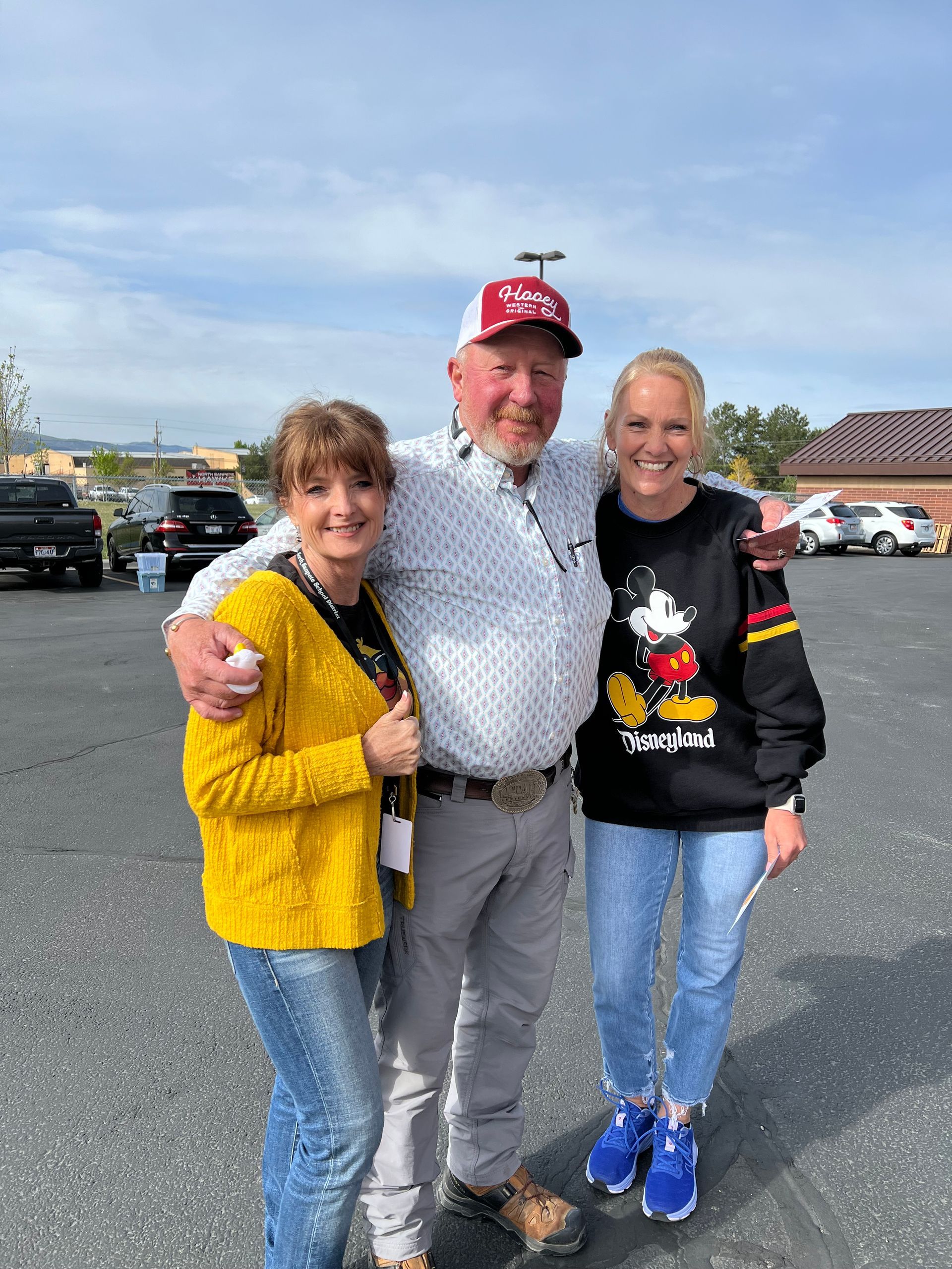 A man and two women are posing for a picture in a parking lot.