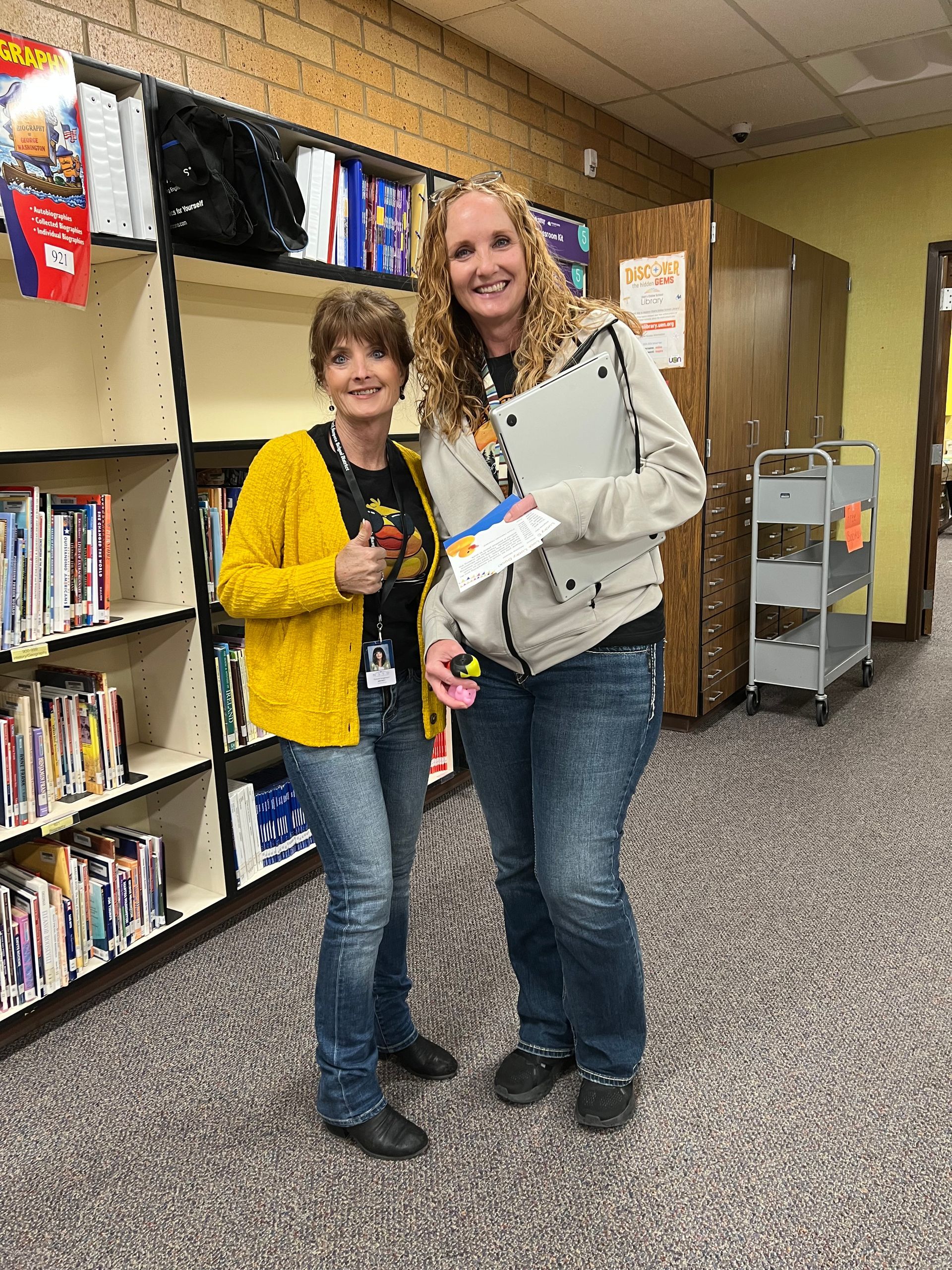 Two women are standing next to each other in a library.