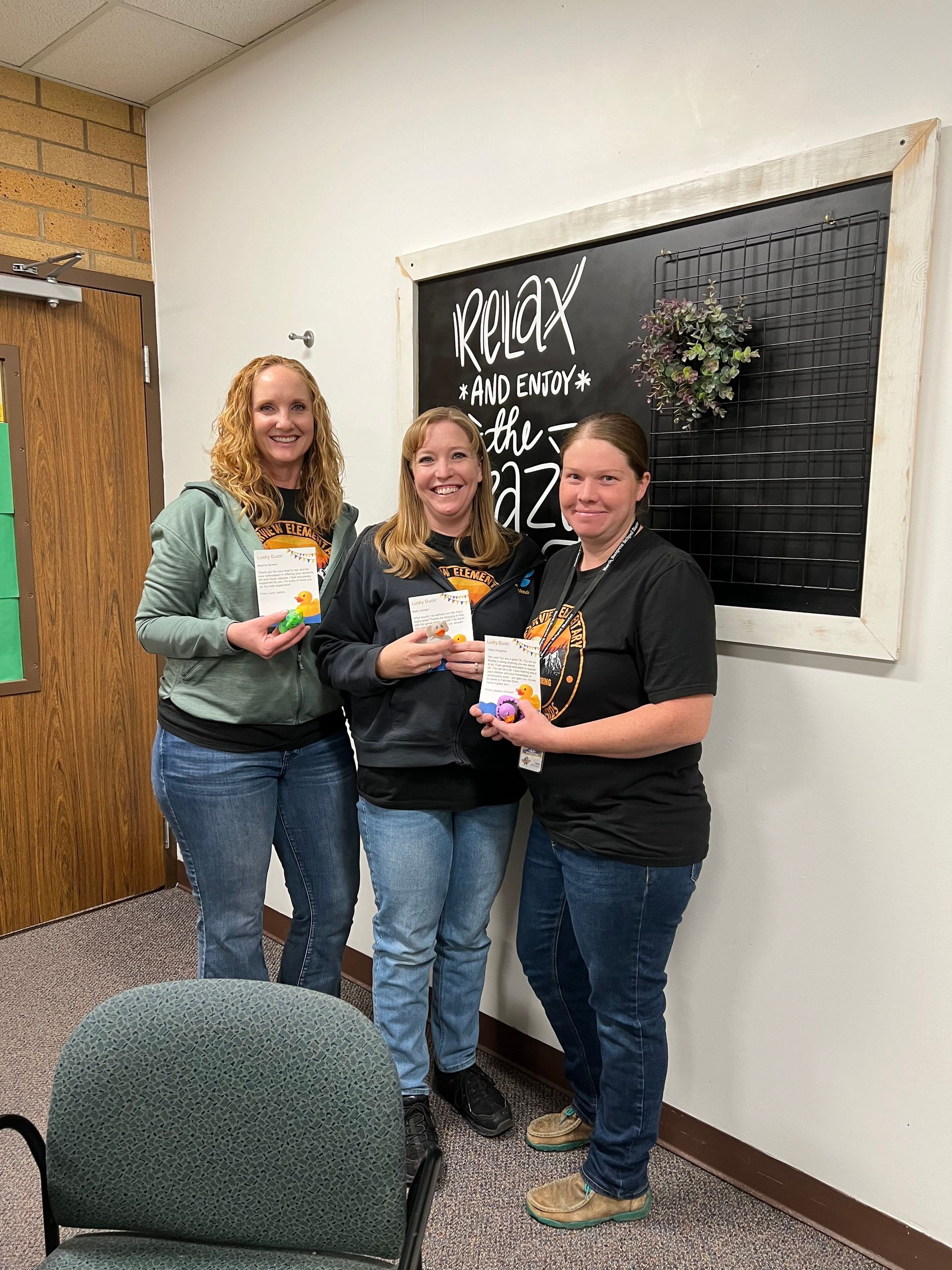 Three women are standing next to each other in a room holding books.