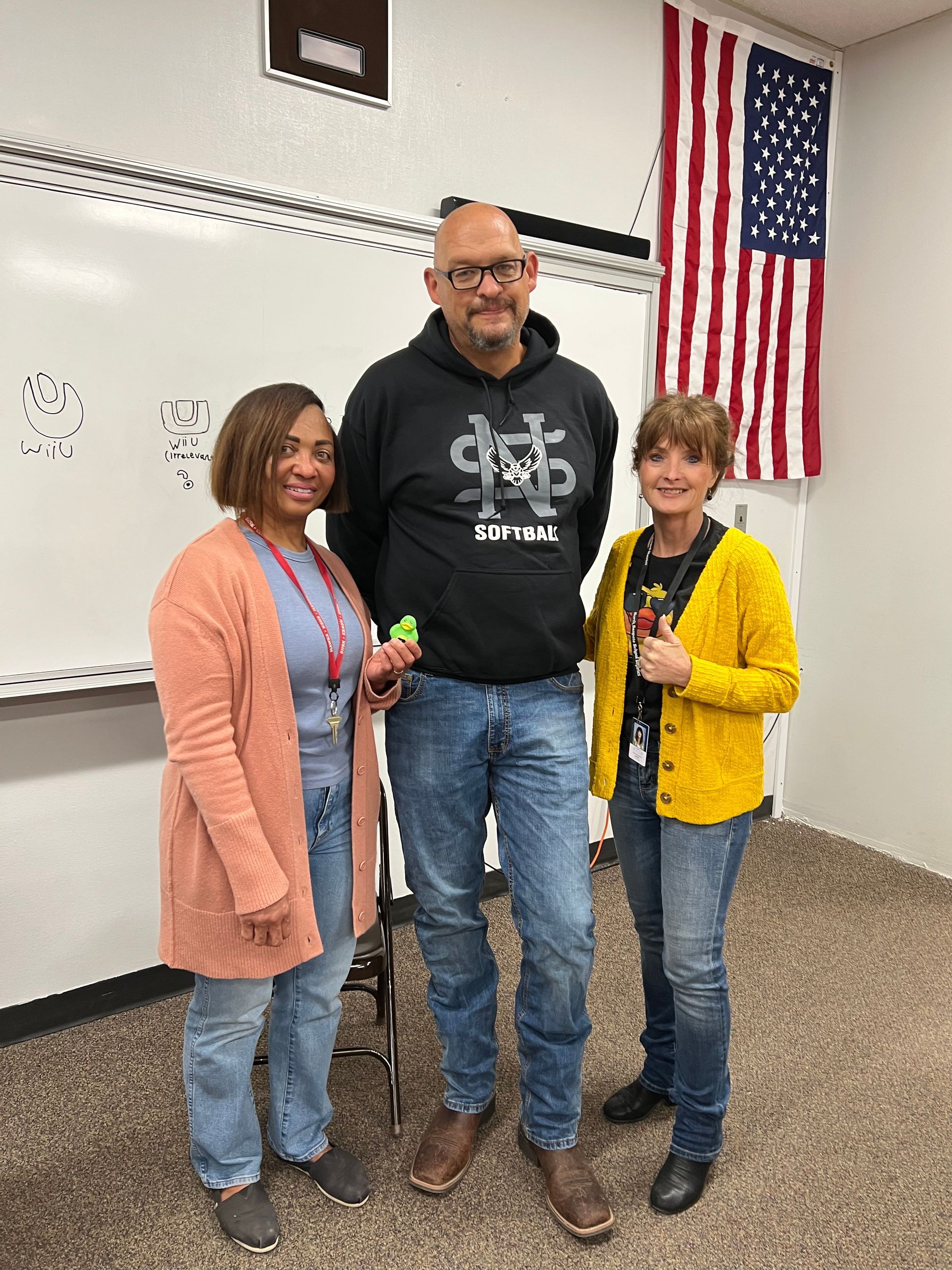 A man and two women are standing next to each other in a classroom.