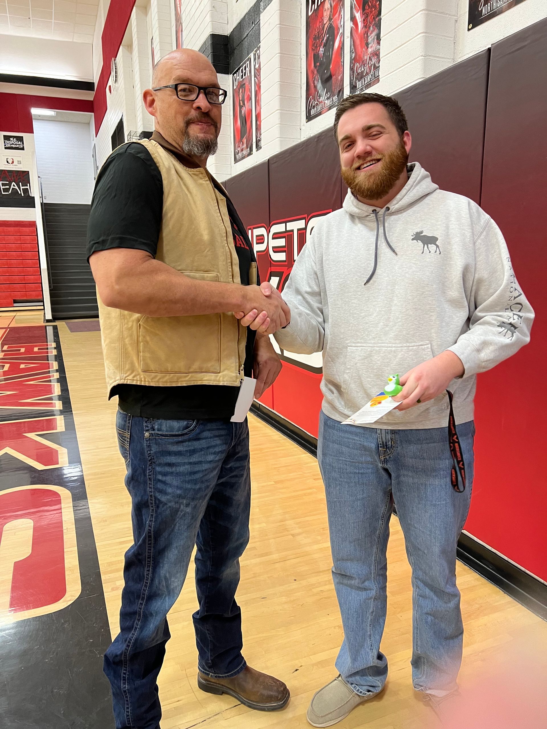 Two men are shaking hands in a gym.