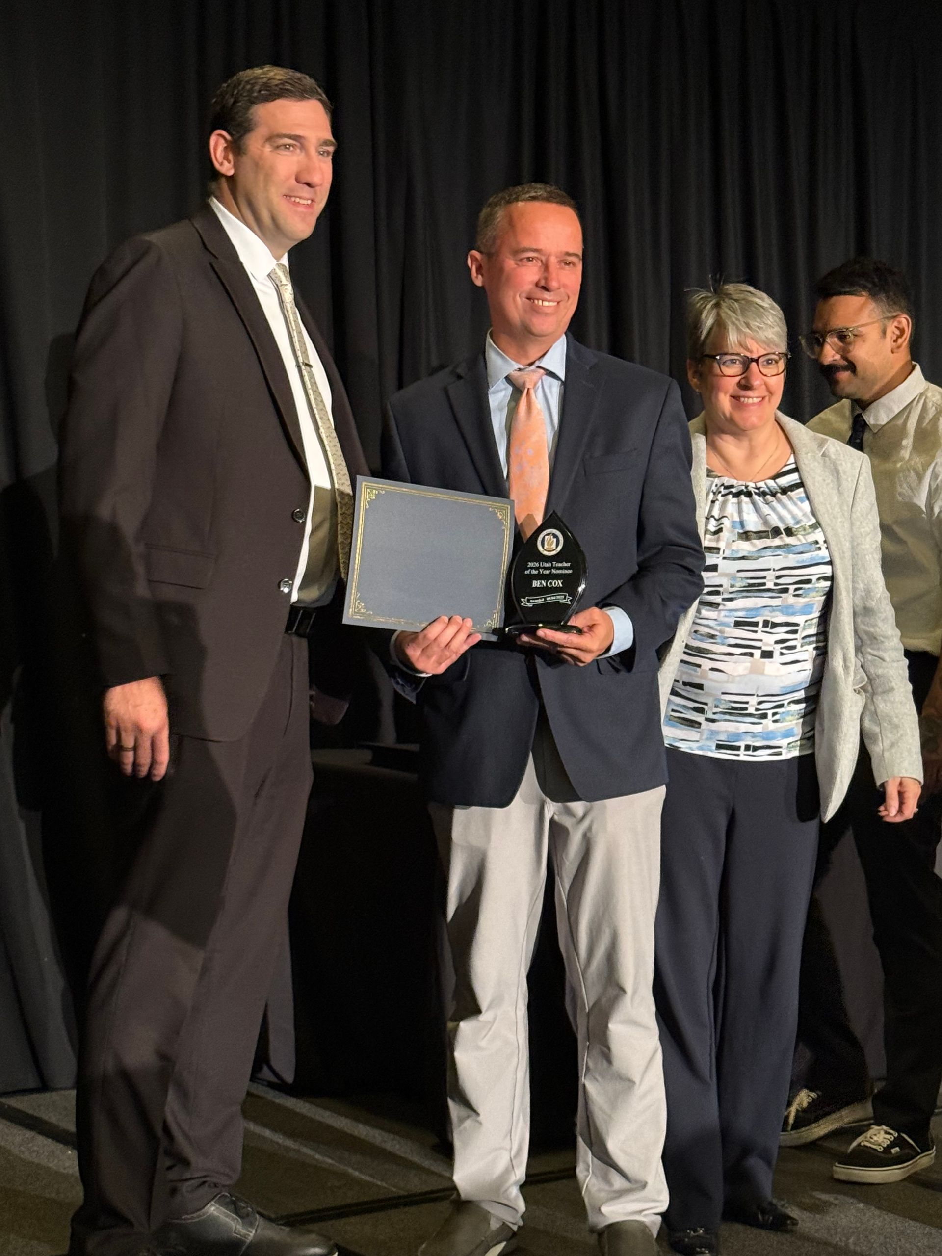 Man in suit holding award, posing with three people on stage.
