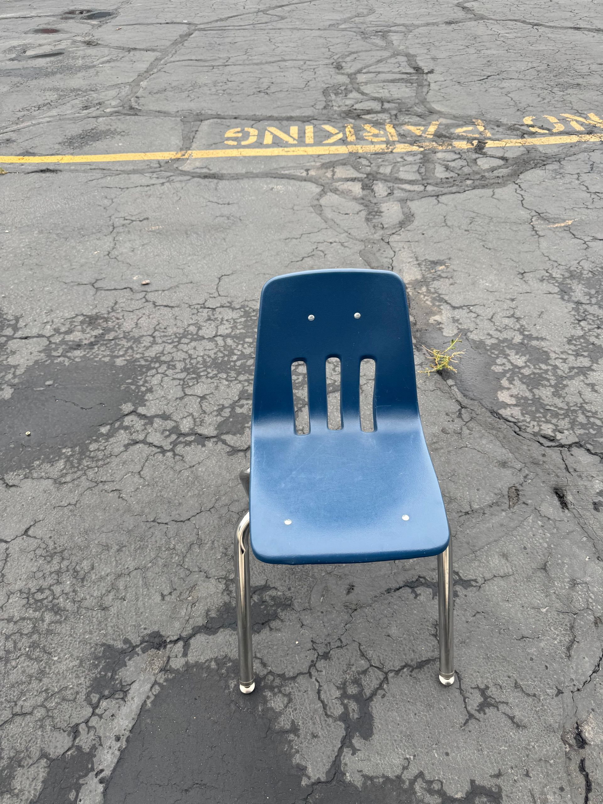 Blue school chair on cracked asphalt parking lot.