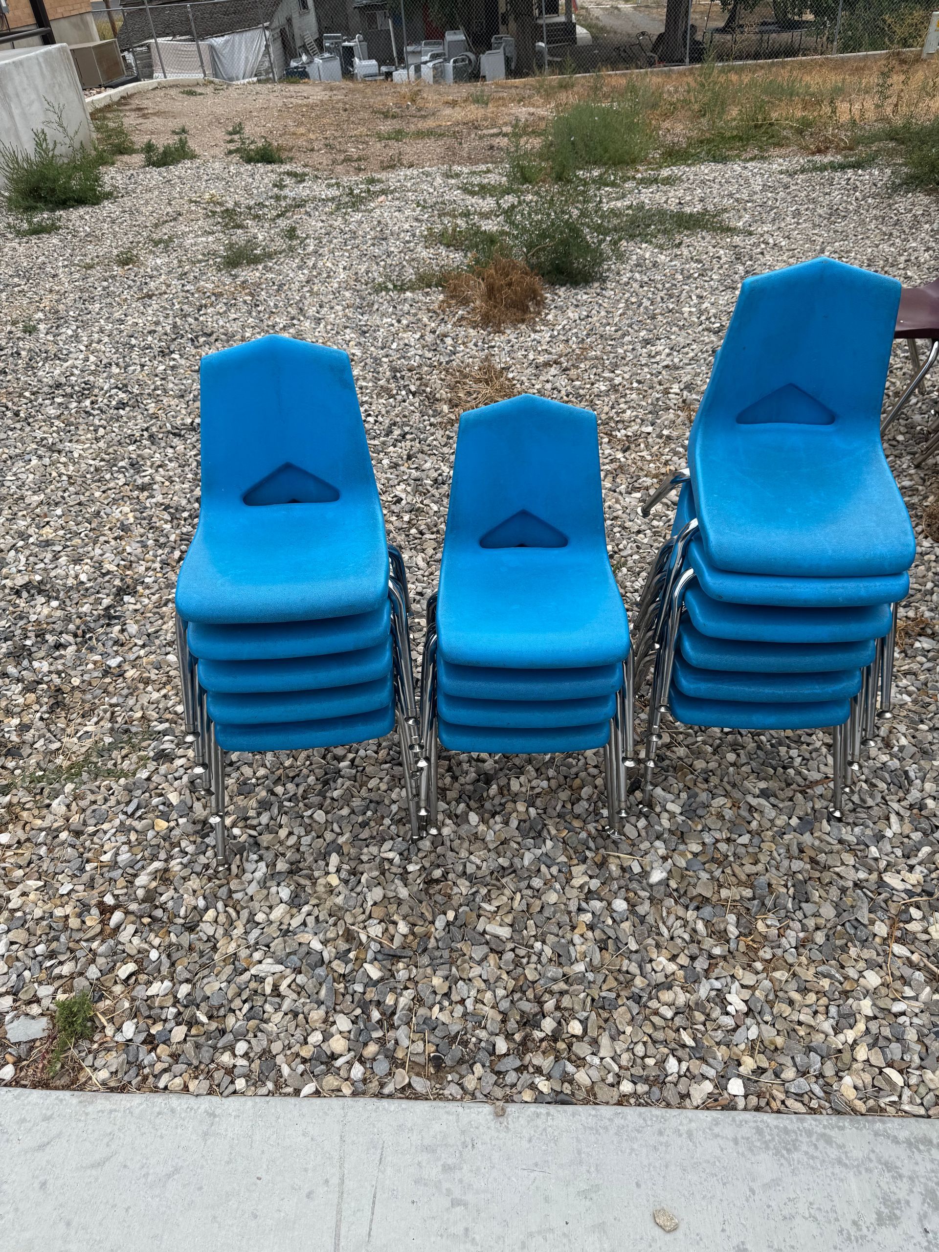 Three stacks of blue plastic chairs on gravel.