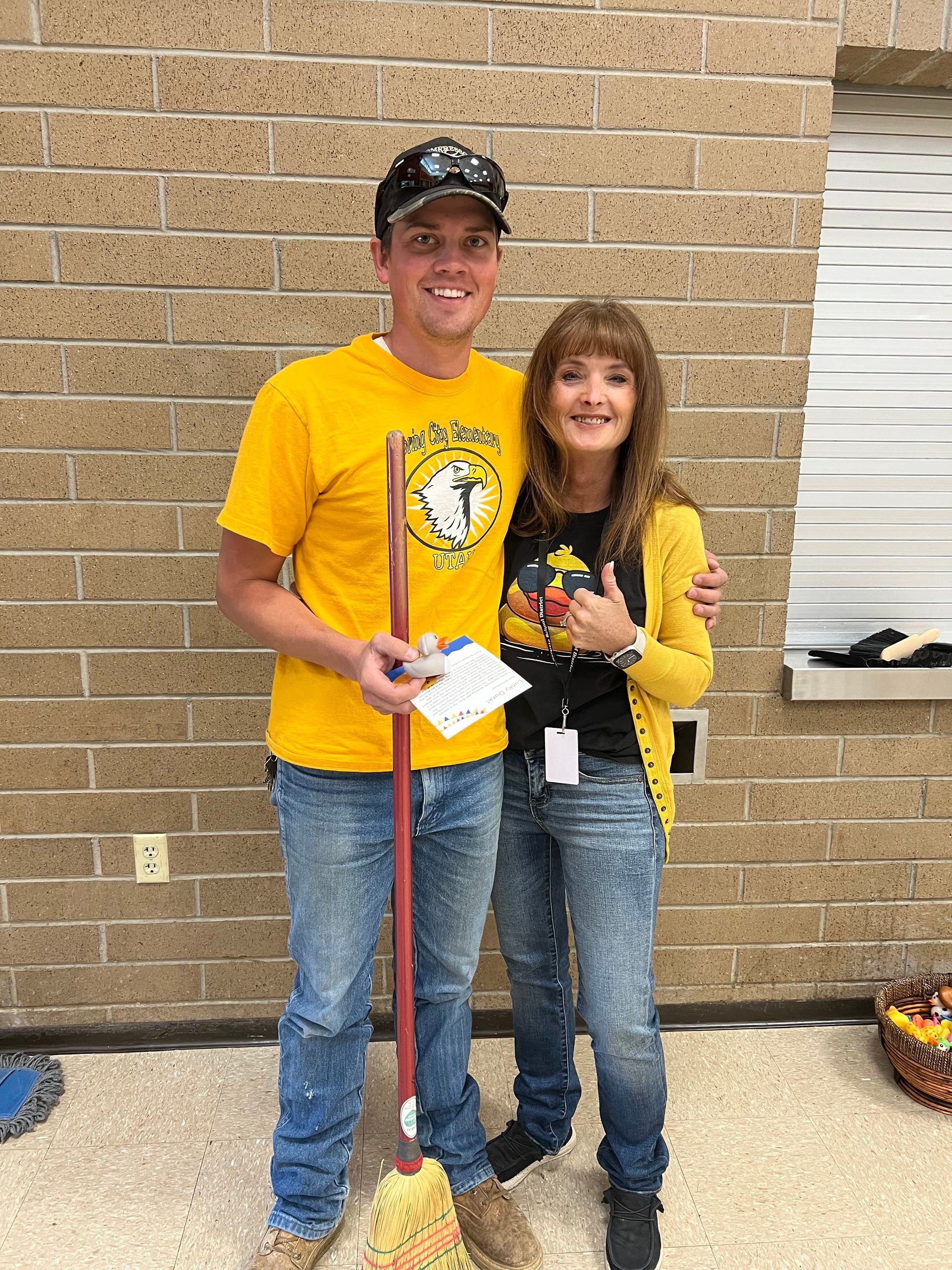 A man in a yellow shirt is standing next to a woman holding a mop.