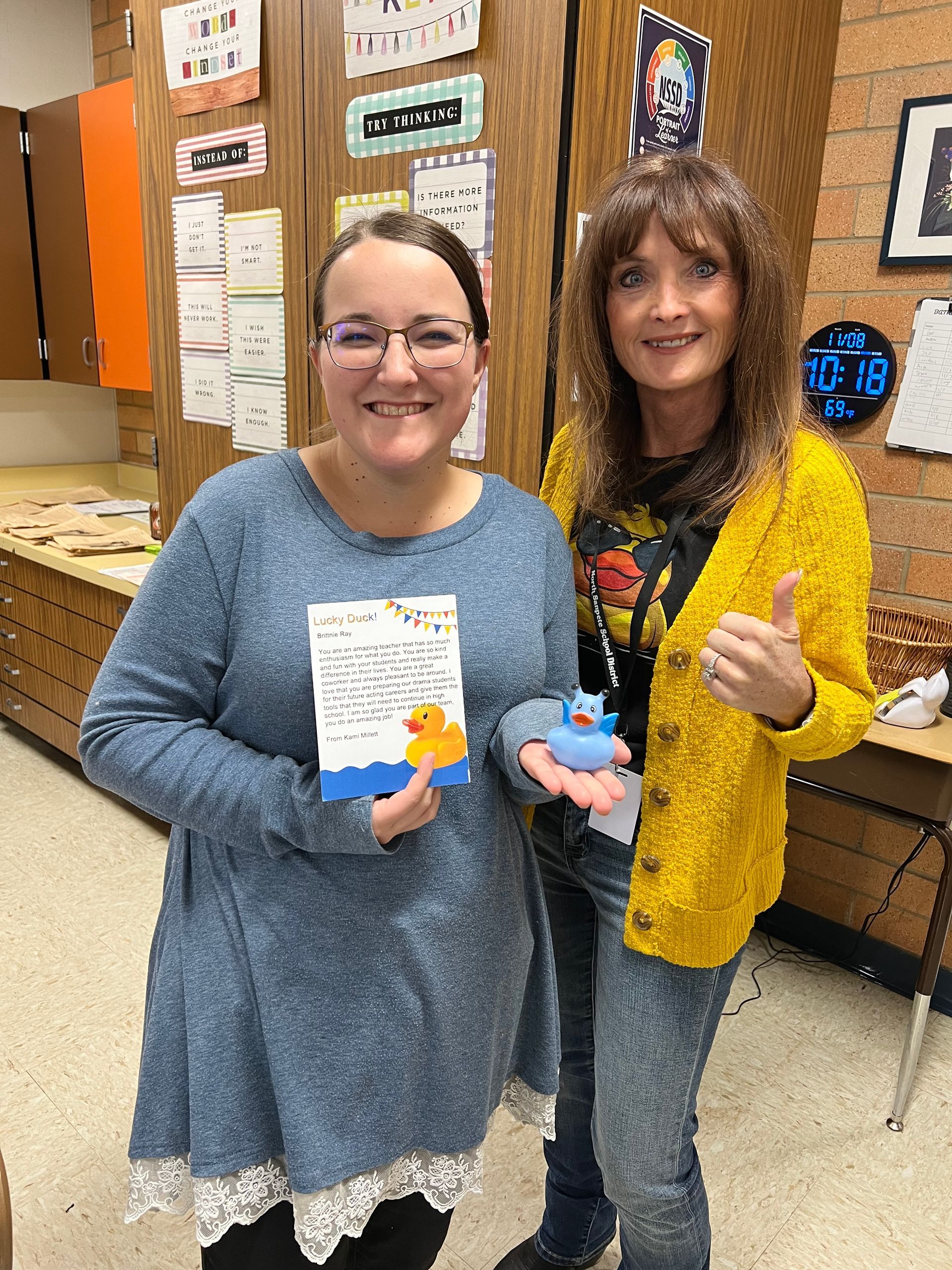 Two women are standing next to each other holding a rubber duck and a book.